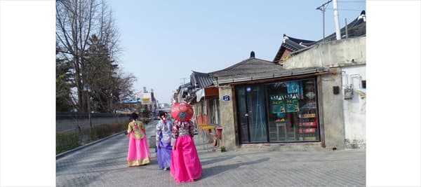 한복을 입은 여성이 길을 걷고 있습니다. 손에 무엇이 들려있나요?